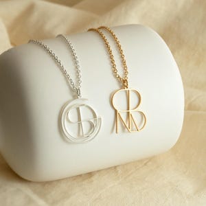 May include: Two delicate necklaces with geometric pendant charms. One necklace features a silver pendant with a circular design, while the other necklace features a gold pendant with a geometric design.