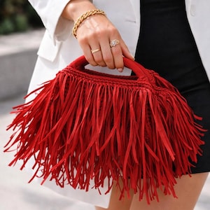May include: A vibrant red handbag with a fringe design. The bag has a structured shape with a handle and is made of a woven material. The fringe detail adds a playful and stylish element to the accessory.