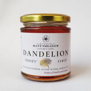Könnte beinhalten: Ein Glasgefäß mit goldenem Deckel, gefüllt mit Löwenzahnhonigsirup. Das Etikett lautet "Maye's Meadow Nature's Gifts Dandelion 'Honey' Syrup Dandelion Flower, Sugar, Water, Lemon Juice Produce of Dumfries and Galloway"