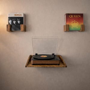 Op de afbeelding: Een houten platenspeler met een doorzichtige deksel staat op een houten plank. Twee houten platenhouders tonen albumhoezen van The Beatles en Queen. De opstelling is gemonteerd op een neutraal gekleurde muur.