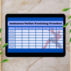 May include: A black tablet displays a blue and white "Jacksons Toilet Training Tracker." The tracker has a grid for daily entries, with a Spider-Man graphic. The tablet is set against a marble background with green leaf accents.