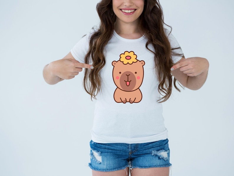 May include: White t-shirt featuring a cartoon bear with a flower on its head. The bear is brown with a pink nose and tongue. The shirt is paired with denim shorts.