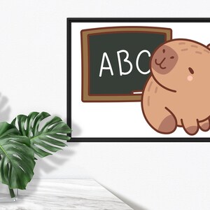 May include: A framed print featuring a cartoon illustration of a brown capybara next to a chalkboard with the letters "ABC". The artwork has a white background and is framed in black. A green plant in a clear vase is in the foreground.