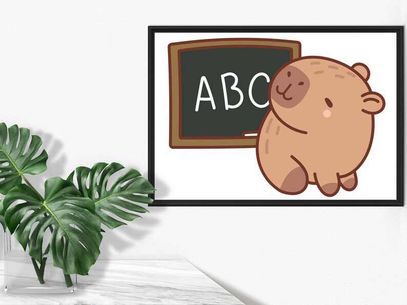 May include: A framed print featuring a cartoon illustration of a brown capybara next to a chalkboard with the letters "ABC". The artwork has a white background and is framed in black. A green plant in a clear vase is in the foreground.