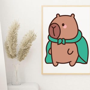May include: A framed print featuring a cartoon capybara wearing a teal cape and scarf. The capybara is brown with a pink cheek and a dark brown nose. The artwork is displayed on a white wall next to a vase with dried plants.
