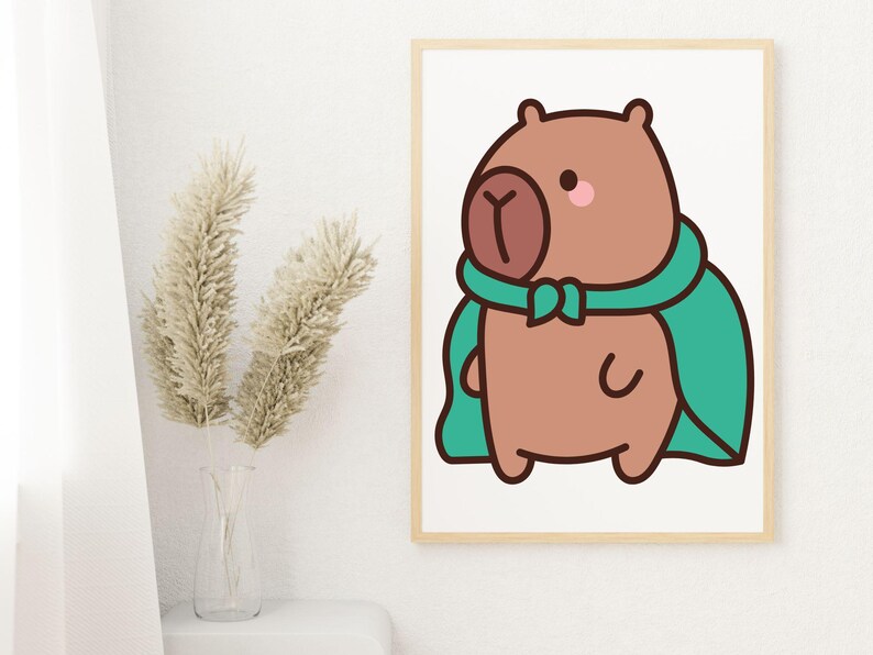May include: A framed print featuring a cartoon capybara wearing a teal cape and scarf. The capybara is brown with a pink cheek and a dark brown nose. The artwork is displayed on a white wall next to a vase with dried plants.