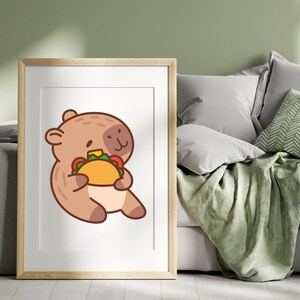 May include: A framed print featuring a cartoon bear holding a taco. The bear is brown with a light brown face and is sitting down. The taco has a yellow shell with green, red, and white fillings. The frame is light brown.
