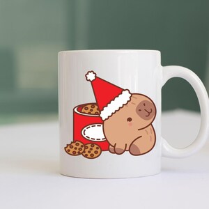 May include: White ceramic mug featuring a cartoon sloth wearing a Santa hat, next to a red cookie tin. The tin is filled with cookies, and a few cookies are scattered in front. A festive holiday design.