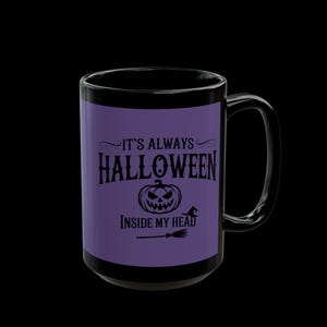 May include: Black ceramic mug with a purple band featuring the text "IT'S ALWAYS HALLOWEEN INSIDE MY HEAD" in black, along with a jack-o'-lantern and witch's hat graphic. The mug has a black handle and rim, perfect for Halloween.
