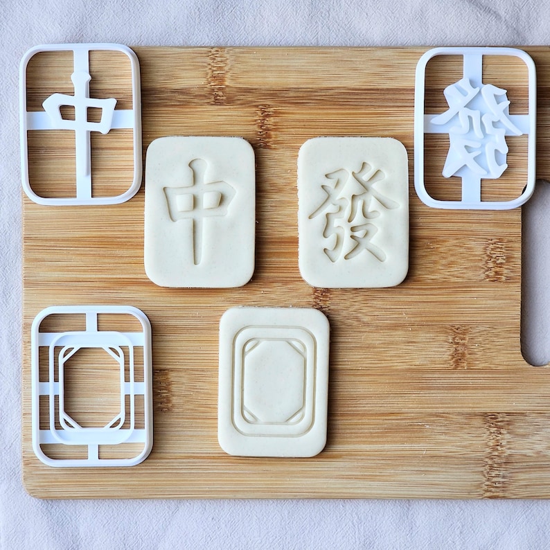 3D printed white plastic cookie cutters are in the shape of Chinese Mahjong Tile characters. The biscuits are rectangular with the Chinese characters imprinted on them.