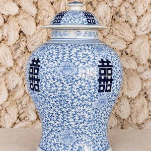 May include: A blue and white porcelain ginger jar with a matching lid. The jar features a dense pattern of scrolling vines and flowers, accented by the double happiness symbol in dark blue on both the body and the lid.