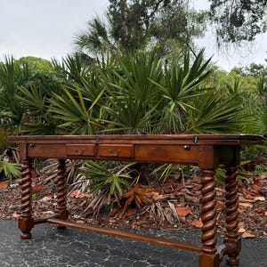 May include: A long, rectangular wooden console table with a warm brown finish. The table features two central drawers with small metal pulls and four distinct barley twist legs connected by a horizontal stretcher base near the floor.