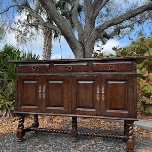 May include: A dark brown antique cabinet with three drawers and four doors. The cabinet has brass ring pulls on the drawers and ornate handles on the doors. The base features carved spiral legs and a matching stretcher.