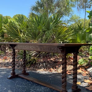 May include: A long, rectangular wooden table featuring a dark brown finish with a visible wood grain. The table is supported by four legs, each carved into a distinct spiral or barley twist design, connected by two horizontal base stretchers.