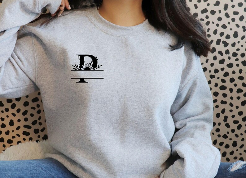 May include: A gray sweatshirt with a black floral design and the letter "D" on the front.