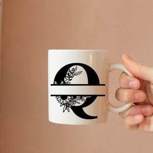 May include: White ceramic mug with a black floral design and the letter Q. The mug has a black line across the middle.