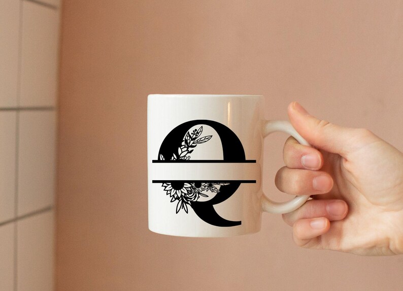 May include: White ceramic mug with a black floral design and the letter Q. The mug has a black line across the middle.
