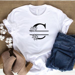 May include: White t-shirt with a black floral design and the letter "C" split in half with a line.