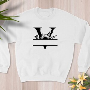 May include: White sweatshirt with a black floral design featuring the letter V and a blank space for a name.