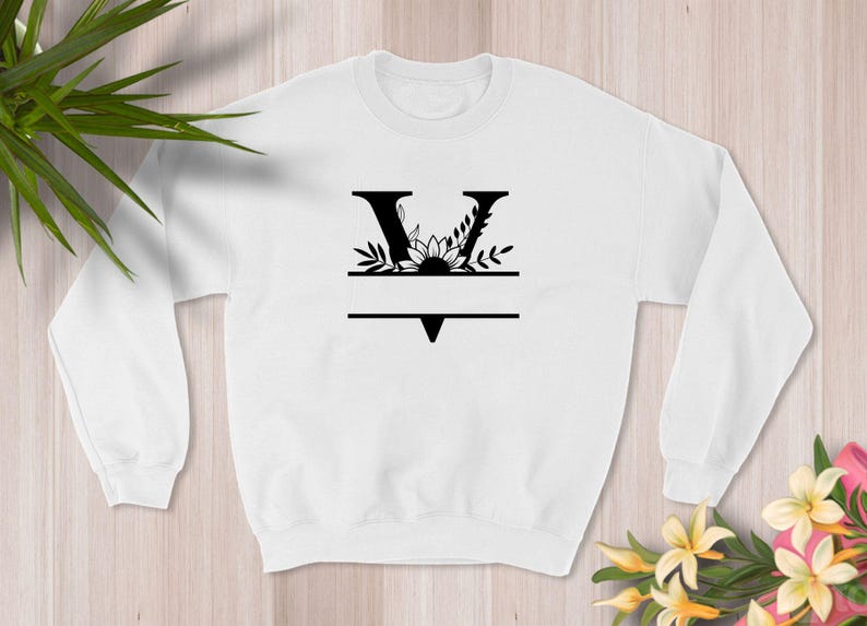 May include: White sweatshirt with a black floral design featuring the letter V and a blank space for a name.