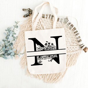 May include: A white canvas tote bag with black floral design around the letter "N".