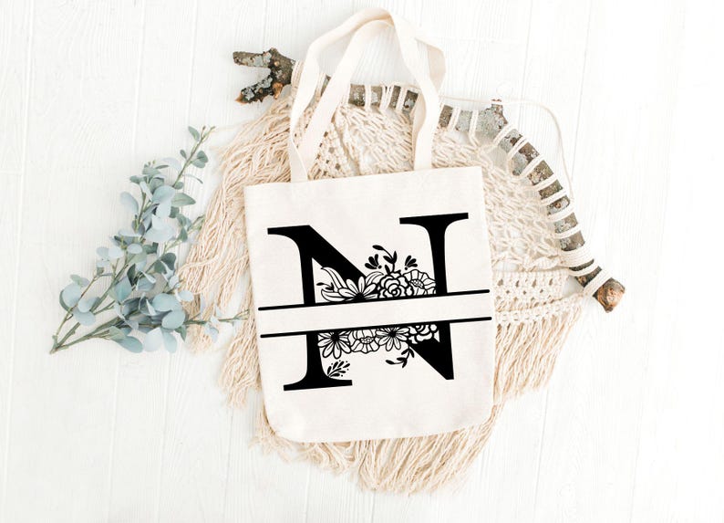 May include: A white canvas tote bag with black floral design around the letter "N".