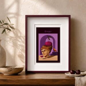 May include: A framed print featuring a surreal illustration of a classical stone head with a large cherry on top, drinking from a glass. The background is purple with an archway and a small orange bird. The text reads Miraggio and Amarena Club.