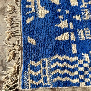 Op de afbeelding: Een blauw en wit geweven tapijt met een geometrisch patroon en franjes aan &eacute;&eacute;n kant.