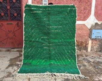 May include: A green and white Moroccan rug with a geometric pattern. The rug has a fringe border and is made of wool.