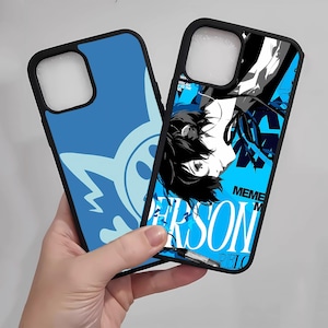 May include: Two black phone cases with blue designs. One case has a light blue character design, and the other features a graphic of a person with the word "PERSON" in white. The cases are held in a hand.