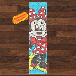 Peut inclure: Un marque-page en crochet représentant une image de dessin animé de Minnie Mouse portant une robe à pois rouges et blancs et un nœud rouge. Le fond est de couleur bleu clair.