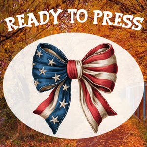 May include: A bow design featuring the American flag, with red and white stripes and blue sections with white stars. The text "READY TO PRESS" is displayed above the bow. The bow is set against a blurred background of autumn leaves.