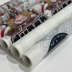 May include: A collection of rolled decorative papers featuring holiday and winter-themed designs. The patterns include gingerbread men, Santa Claus, and the text "Cruisin' Together". The papers are in various colors, including red, white, and brown.