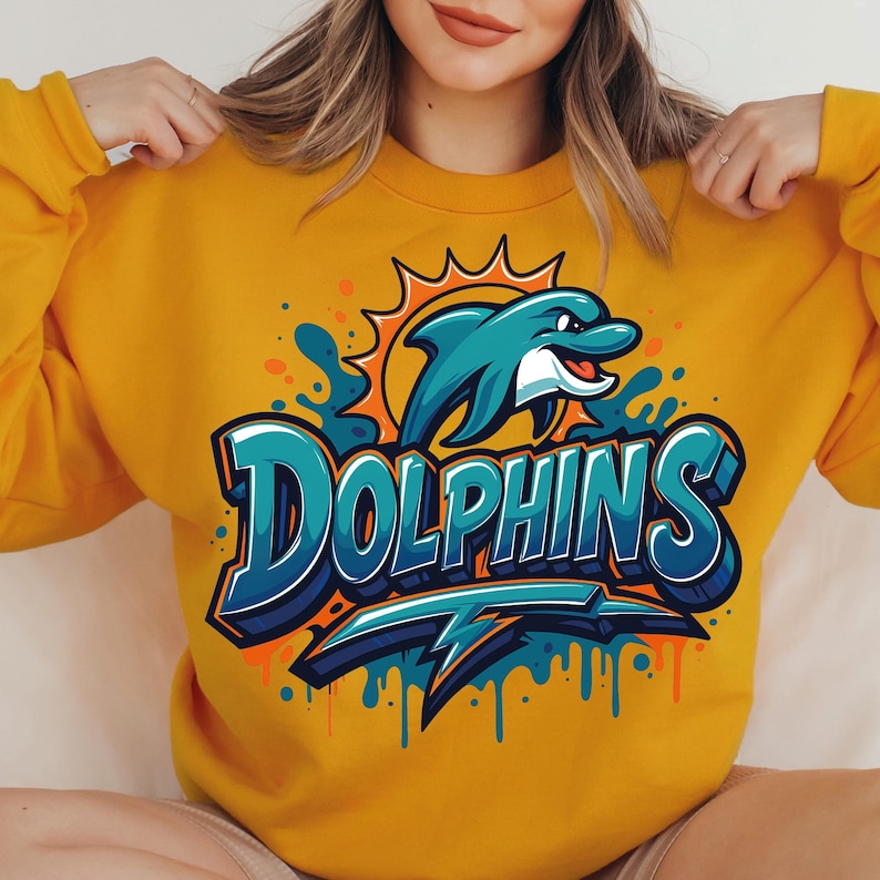 Może przedstawiać: Musztardowa ż&oacute;łta bluza z turkusowym delfinem wyskakującym z wody i napisem "Dolphins" w kolorze turkusowym i białym. Projekt zawiera pomarańczowe akcenty i błyskawicę. Swobodny, sportowy styl.