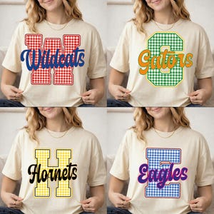May include: A collection of four cream-colored t-shirts, each featuring a large gingham-patterned letter and a team name. The designs include a red W with Wildcats, a green C with Gators, a yellow H with Hornets, and a blue E with Eagles.