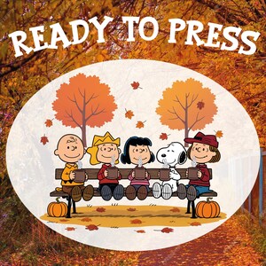 May include: A circular graphic with the text "READY TO PRESS" features the Peanuts gang sitting on a bench, holding mugs of hot beverages. The background includes fall foliage, trees, pumpkins, and falling leaves, creating a cozy autumn scene.
