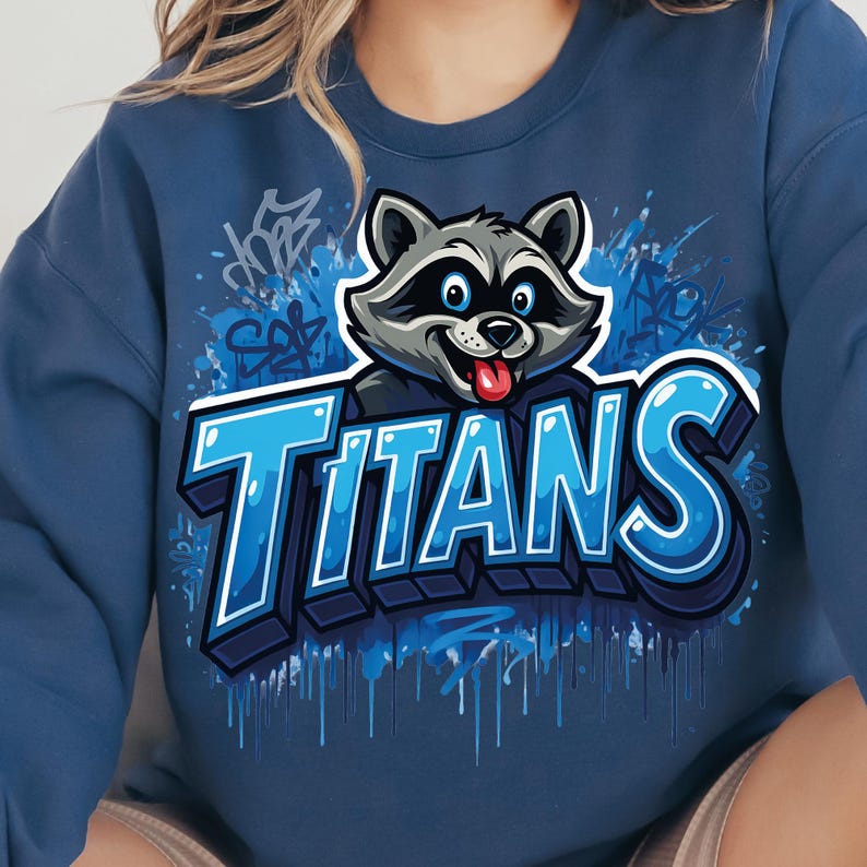 Może przedstawiać: Granatowa bluza z kapturem z kresk&oacute;wkowym szopem i napisem "Titans" w niebieskiej czcionce w stylu graffiti. Szop ma szare futro, niebieskie oczy i czerwony język. Niebieskie plamy farby i graffiti otaczają tekst.