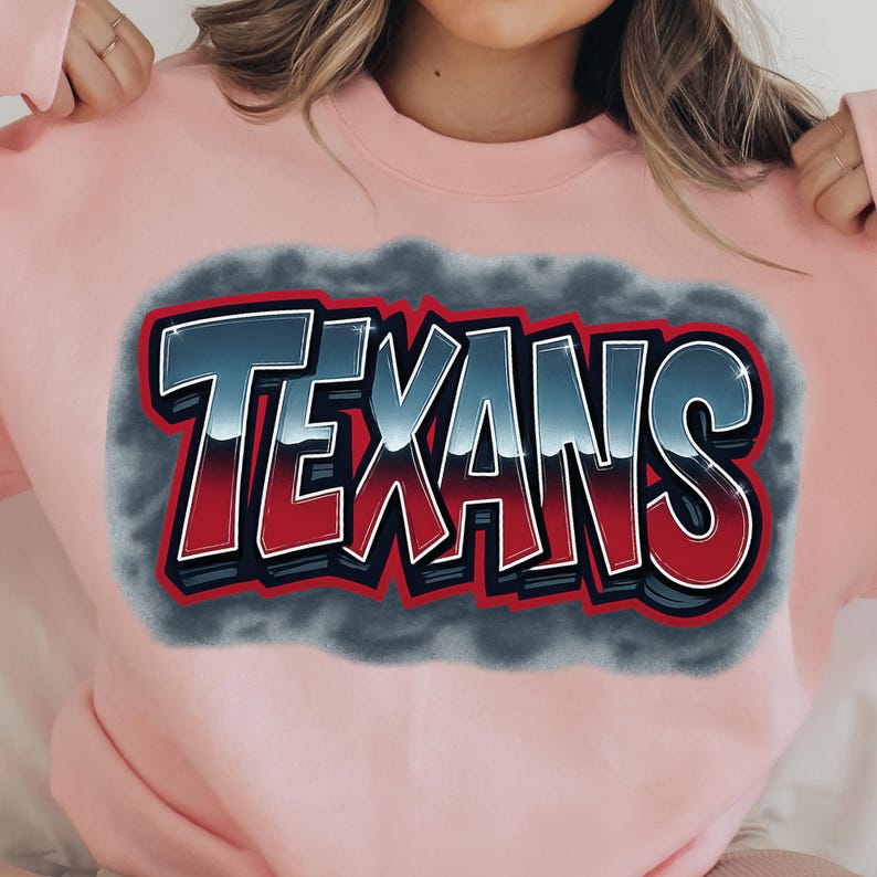 K&ouml;nnte beinhalten: Hellrosa Sweatshirt mit dem Wort "TEXANS" in einem auff&auml;lligen Graffiti-Stil. Der Text ist in einem Blau-Rot-Verlauf mit wei&szlig;er Umrandung gehalten und vor einem grauen, wolkenartigen Hintergrund platziert.