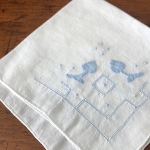 May include: White cotton handkerchief with a blue embroidered design of three stylized hearts and a geometric pattern around the border.