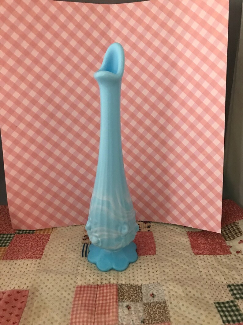 Puede incluir: Un jarr&oacute;n alto de vidrio azul claro con base acampanada y cuello esbelto. El jarr&oacute;n tiene una abertura curva &uacute;nica en la parte superior y detalles decorativos cerca de la base. El jarr&oacute;n mide aproximadamente 30 cm de altura.