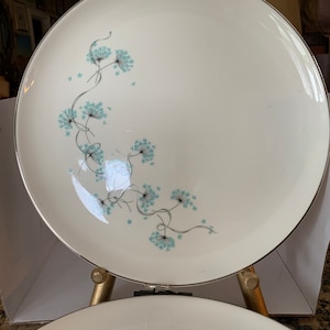 May include: Two white ceramic dinner plates with a silver rim and a blue floral design. The plates are stacked on top of each other.
