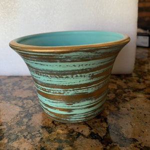 May include: A turquoise and gold ceramic planter with a striped pattern. The planter has a wide mouth and a narrow base.