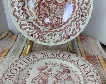 May include: Two decorative plates with a red and white design. The top plate says "Merry Christmas 1997" and features children. The bottom plate says "Good Mother Makes A Happy Home 1973" with children and flowers.
