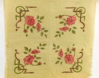 May include: A square, light yellow fabric with a floral pattern. The design features four sets of pink roses with green leaves and decorative green and brown corner accents. The fabric is hanging from two metal clips.