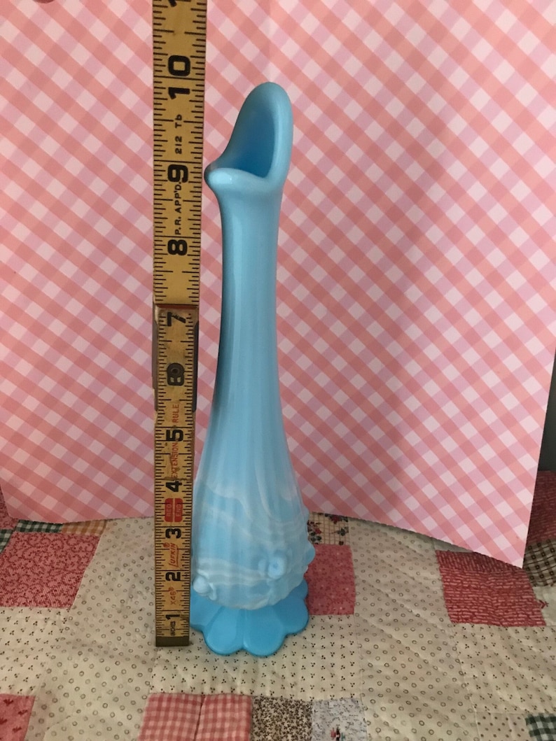 Puede incluir: Un jarr&oacute;n de cristal azul claro con base acampanada y cuello largo y delgado. El jarr&oacute;n mide aproximadamente 25 cm de alto. El jarr&oacute;n tiene una abertura curva &uacute;nica en la parte superior y una base decorativa festoneada. Es una pieza vintage.