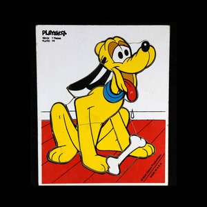May include: A Playskool wooden puzzle featuring Pluto, a yellow dog with black ears and a red tongue. The puzzle has 7 pieces and is made in the USA. The puzzle is on a red background with a white bone.