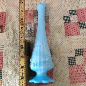 Puede incluir: Un jarr&oacute;n de cristal azul claro, de aproximadamente 25 cm de altura, con base acampanada y parte superior con volantes. El jarr&oacute;n tiene una secci&oacute;n media bulbosa con detalles decorativos. El color es un azul suave y opaco con sutiles vetas blancas.