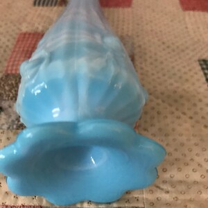 Puede incluir: Un jarr&oacute;n de cristal azul claro con base acampanada y cuello largo y delgado. El jarr&oacute;n tiene un dise&ntilde;o con volantes y texturizado y un acabado suave y opalino. El jarr&oacute;n est&aacute; sobre una tela estampada.