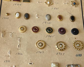 May include: A vintage F. Ronci Co. display card featuring an assortment of metal shoe buckles and ornaments in various shapes, colors, and styles. The card includes handwritten model numbers beneath each item, showcasing decorative metal pieces.