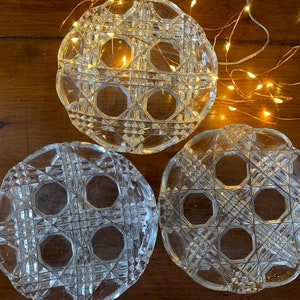 May include: Three clear glass decorative plates with a geometric pattern. The plates are round and have a raised edge. The plates are on a wooden surface.